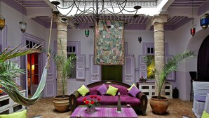 A room with a purple sofa, a hanging tapestry, and potted plants. - Casa Lila & Spa (Essaouira)