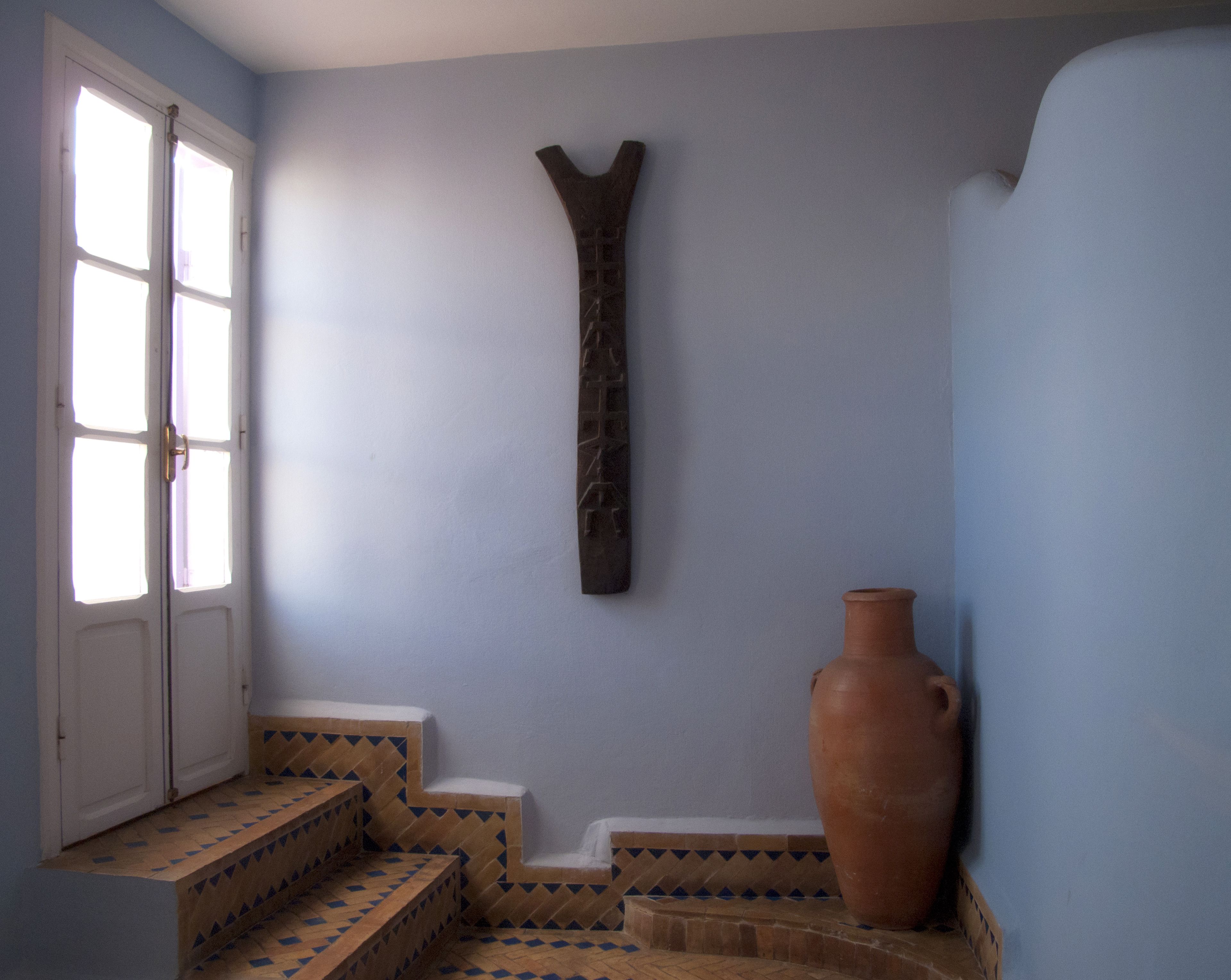 A room with a large window, a wall-mounted wooden cross, and a terracotta vase.