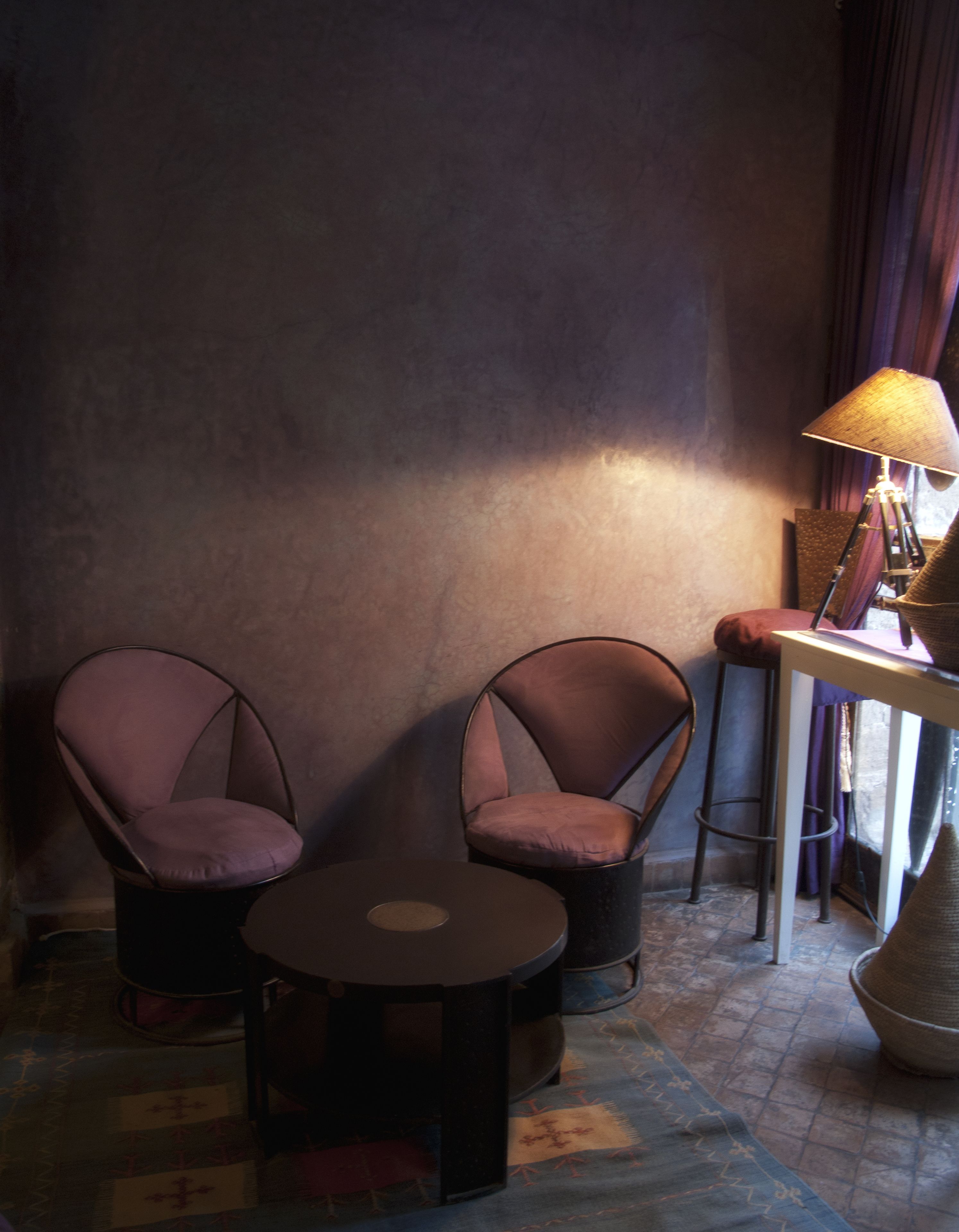 A room with two armchairs, a small round table, a lamp, and a stool.