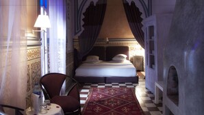 A room with a bed, a chair, a table with a water bottle, and a patterned rug. - Casa Lila & Spa (Essaouira)