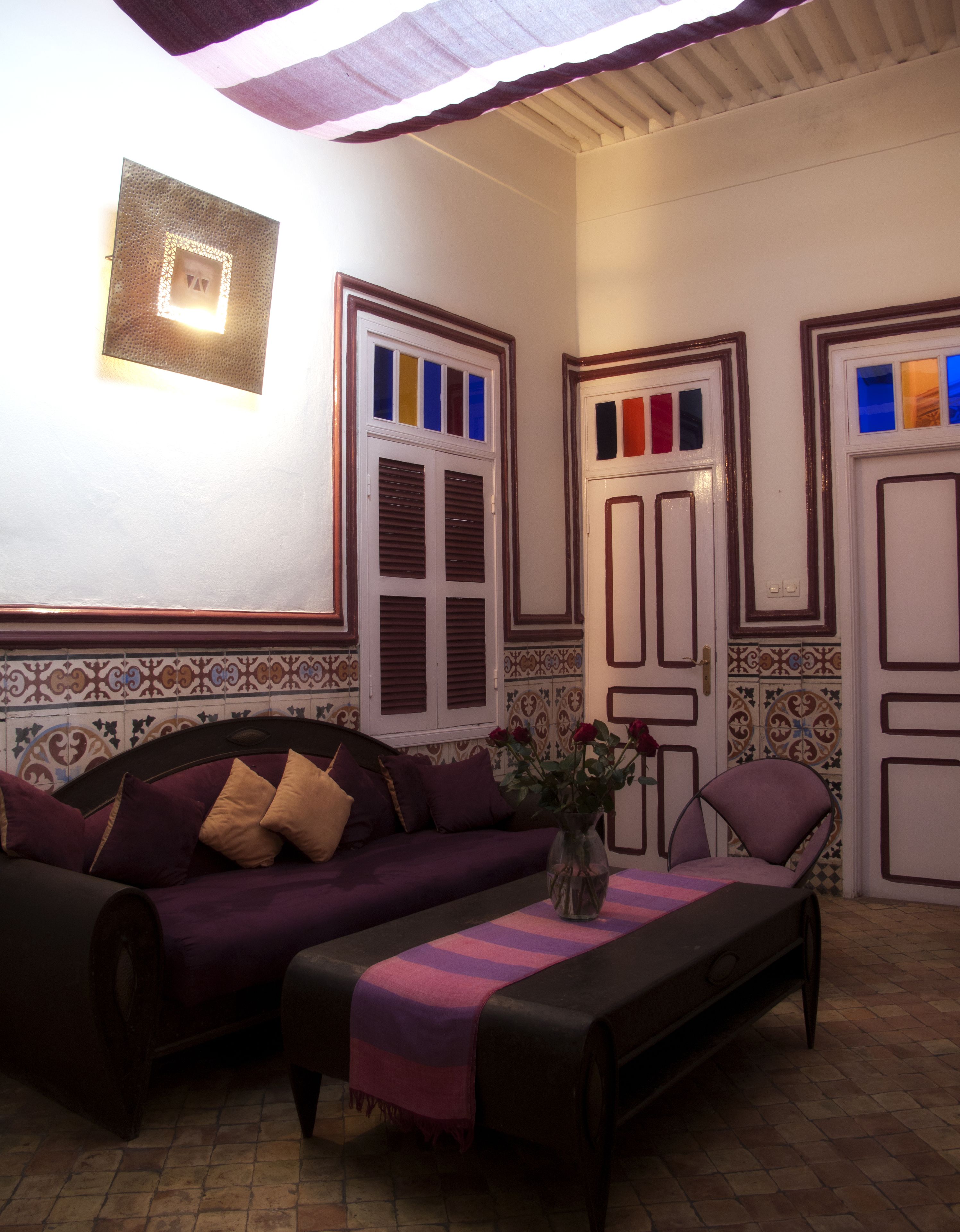 Una sala de estar acogedora con un sofá, una mesa de centro y una silla. Hay azulejos decorativos en las paredes y una pequeña mesa con un florero.