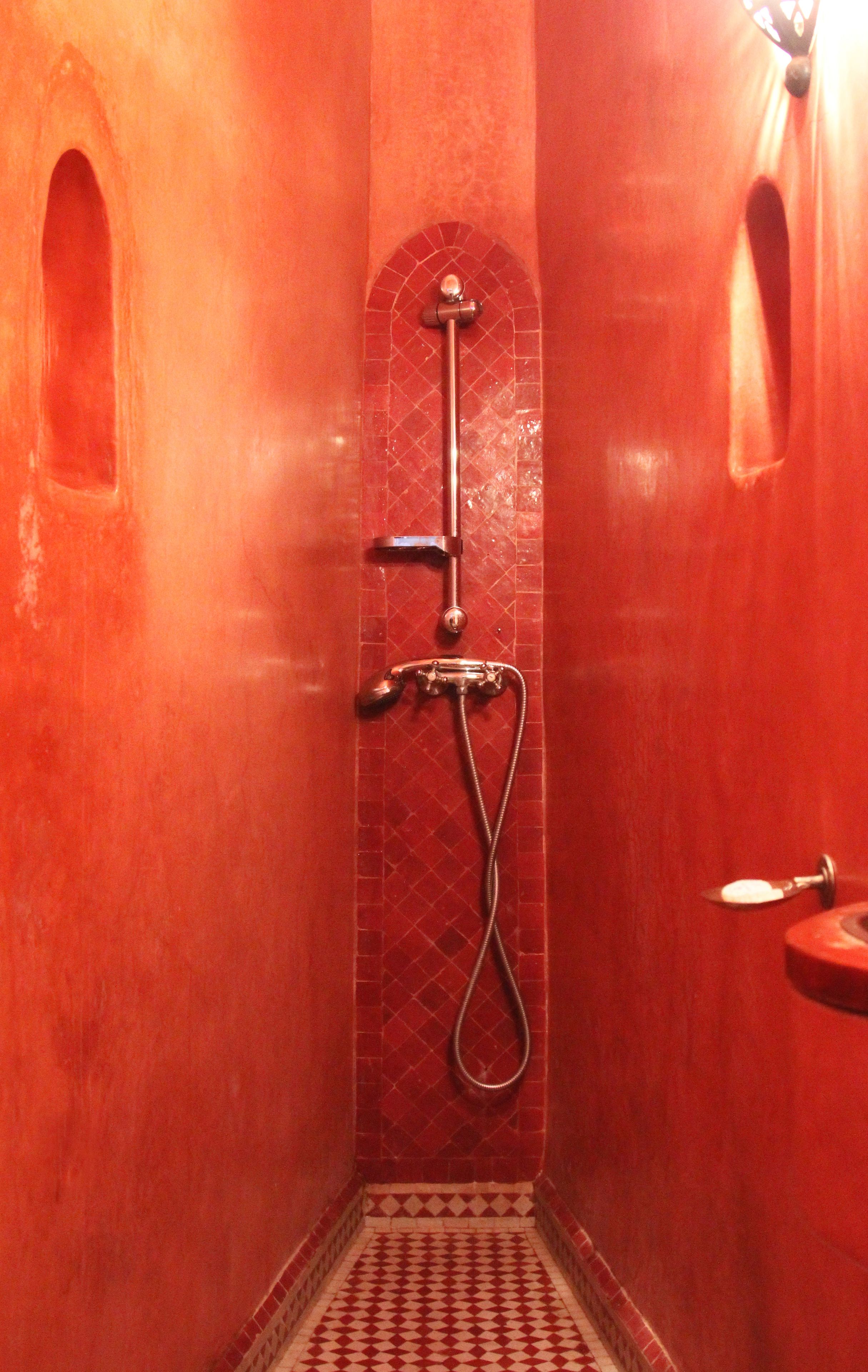 A small, red-tiled bathroom with a shower, a toilet, and a sink.