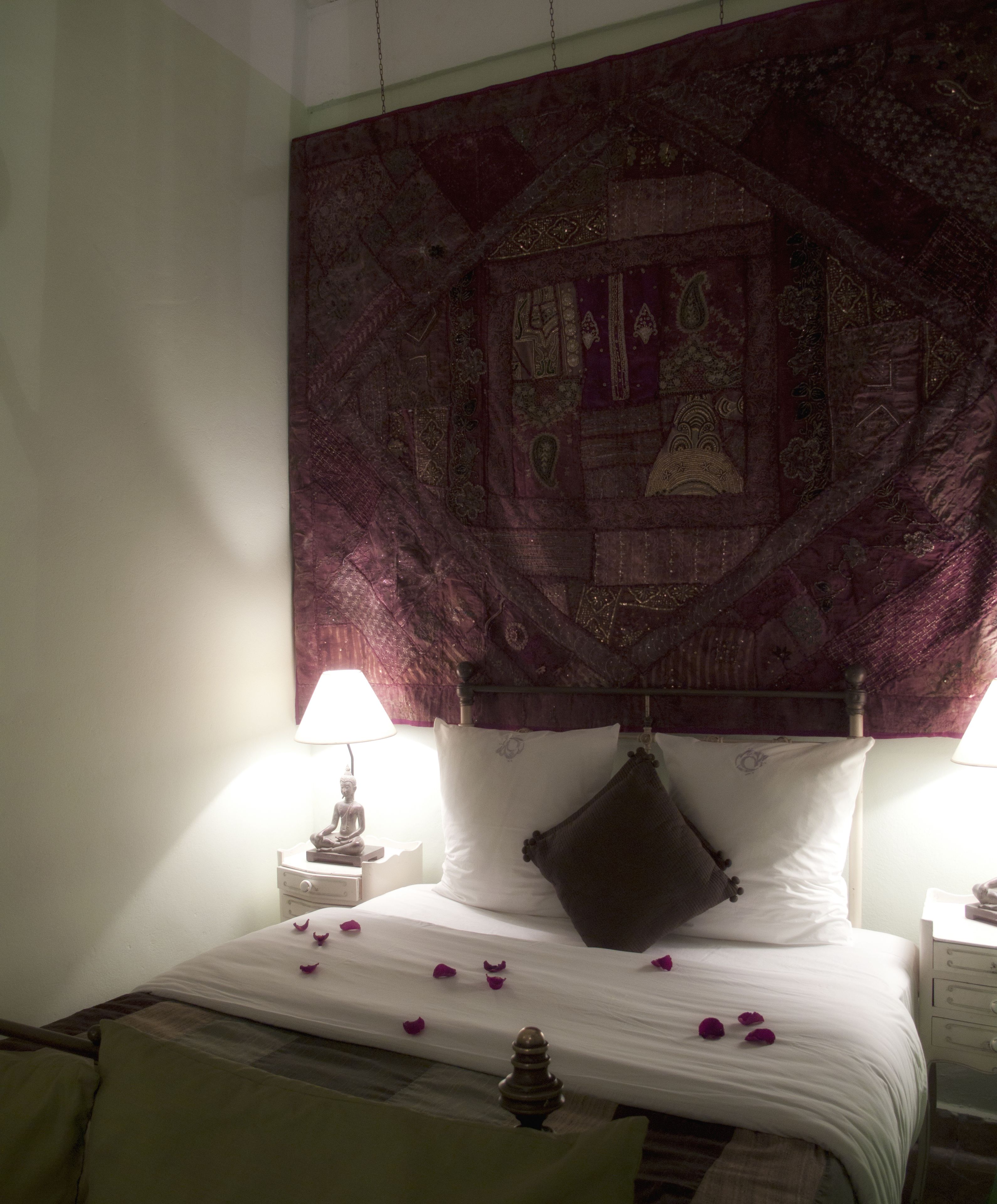 A bedroom with a bed, a tapestry, a nightstand, a lamp, and a statue.