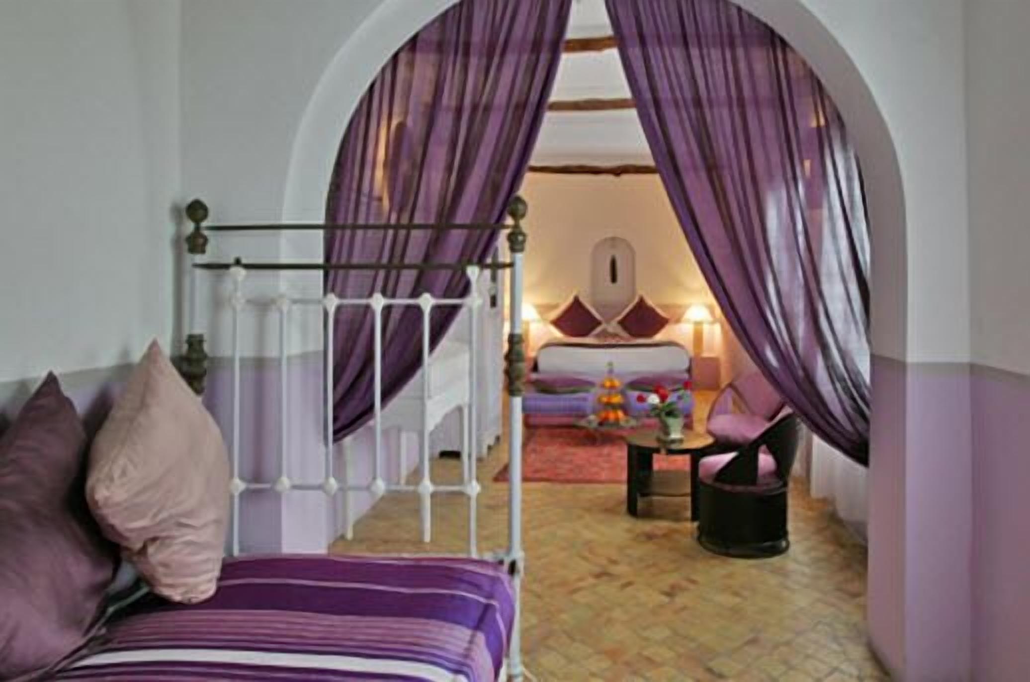 A bedroom with a bed, purple curtains, and a small table with a chair.