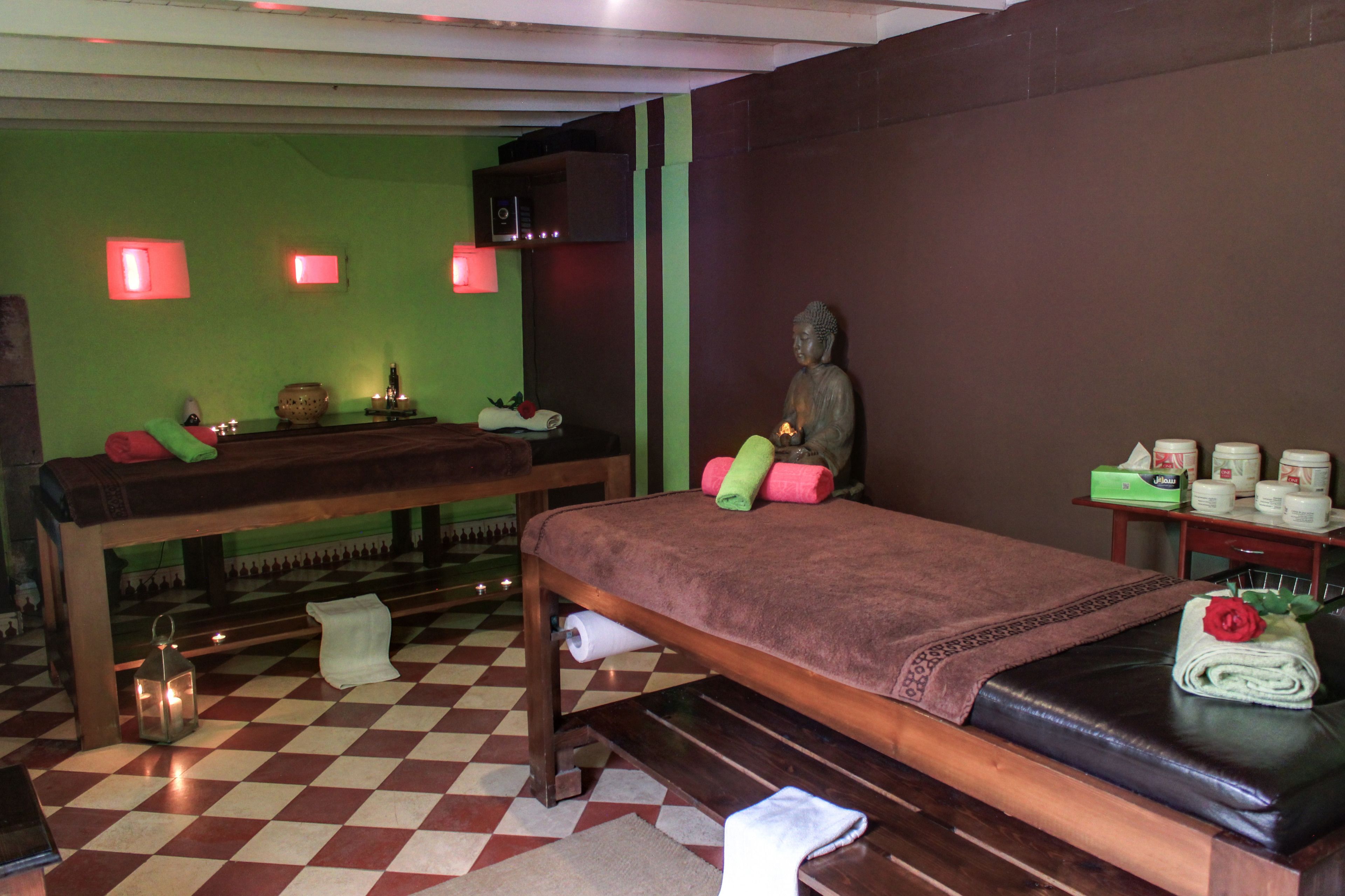 Une salle de spa avec un sol à carreaux, une table de massage, une statue et un petit autel orné de bougies et d’un récipient.
