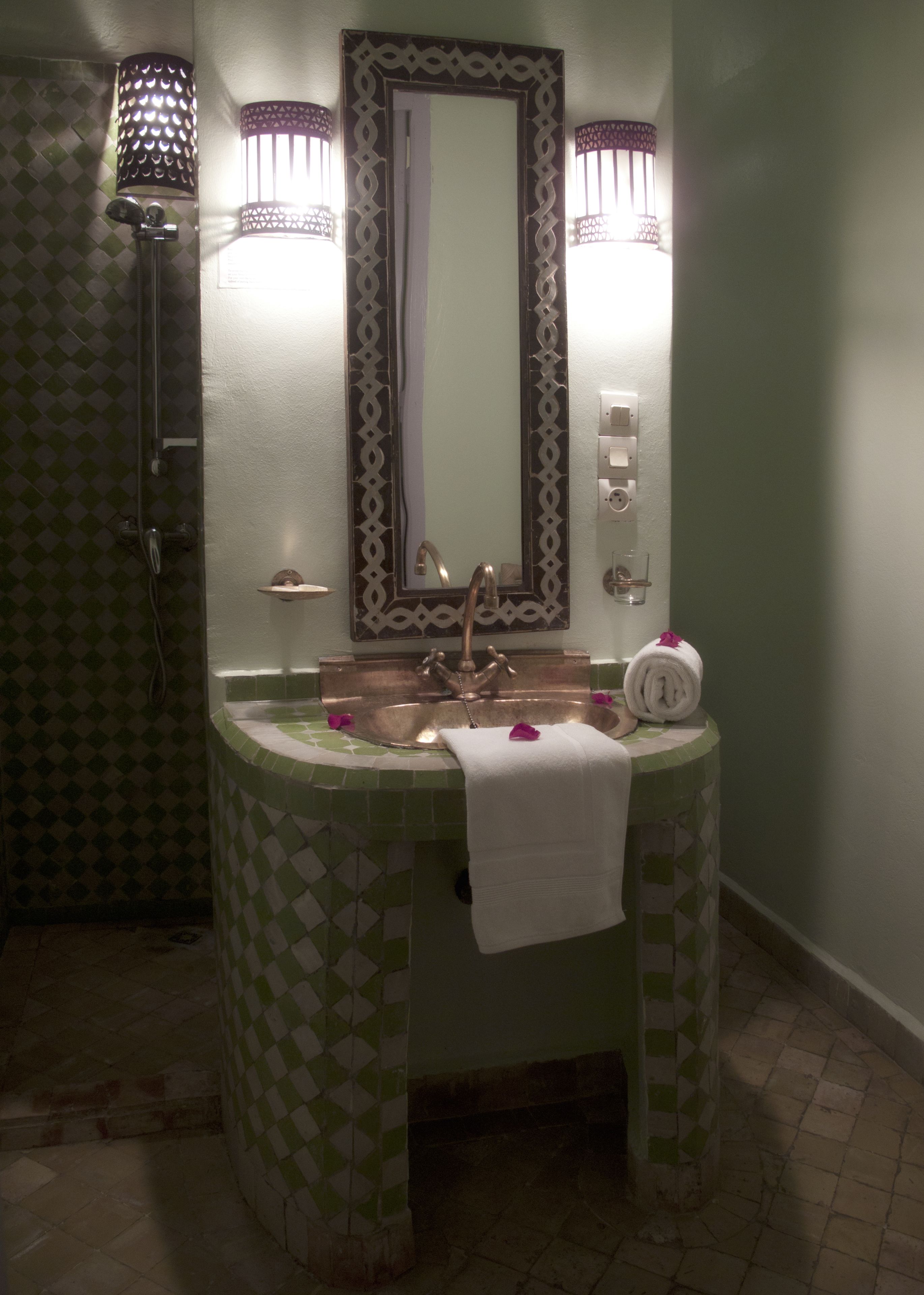 A bathroom with a green and white checkered tile pattern, a sink with a towel, and a mirror with decorative lights.