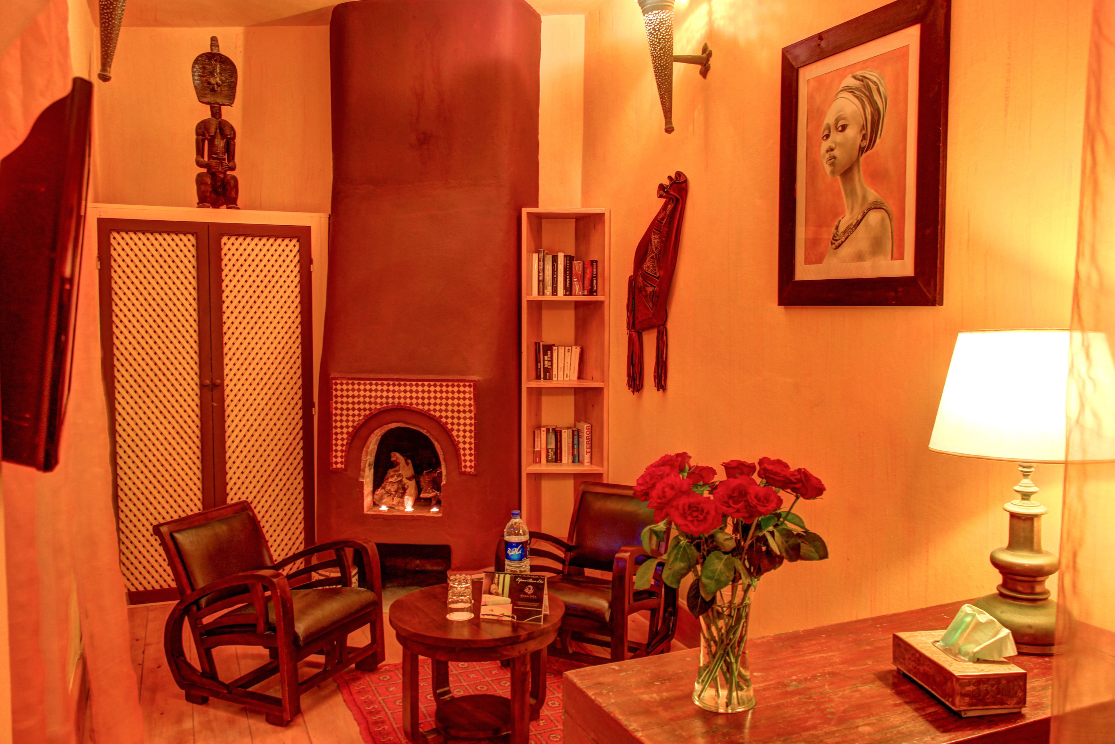 A warmly lit room with a fireplace, bookshelves, a framed portrait, and a vase with red roses.