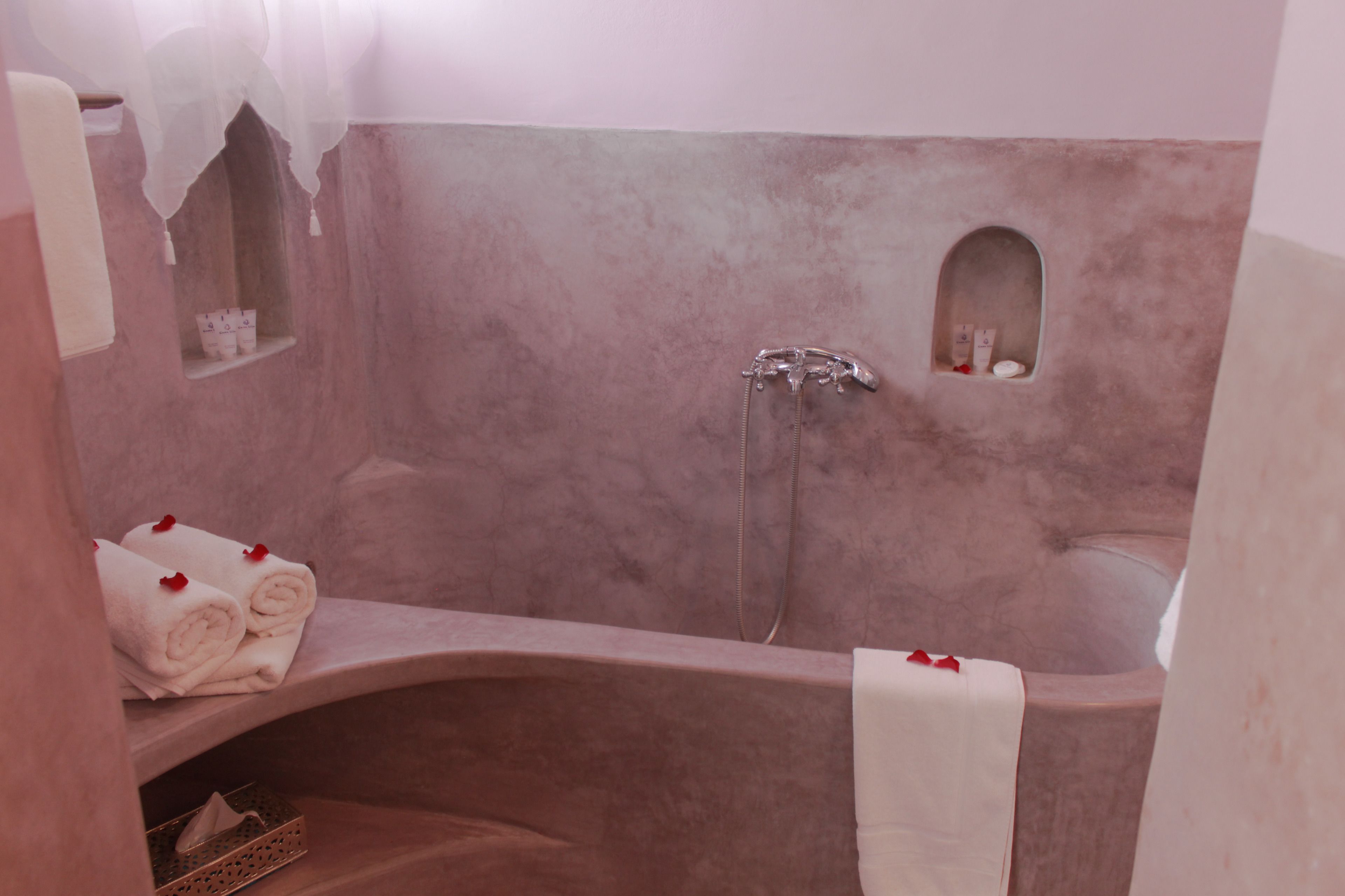 A bathroom with a large bathtub, a shower, and a small window. There are towels and toiletries on the shelves.