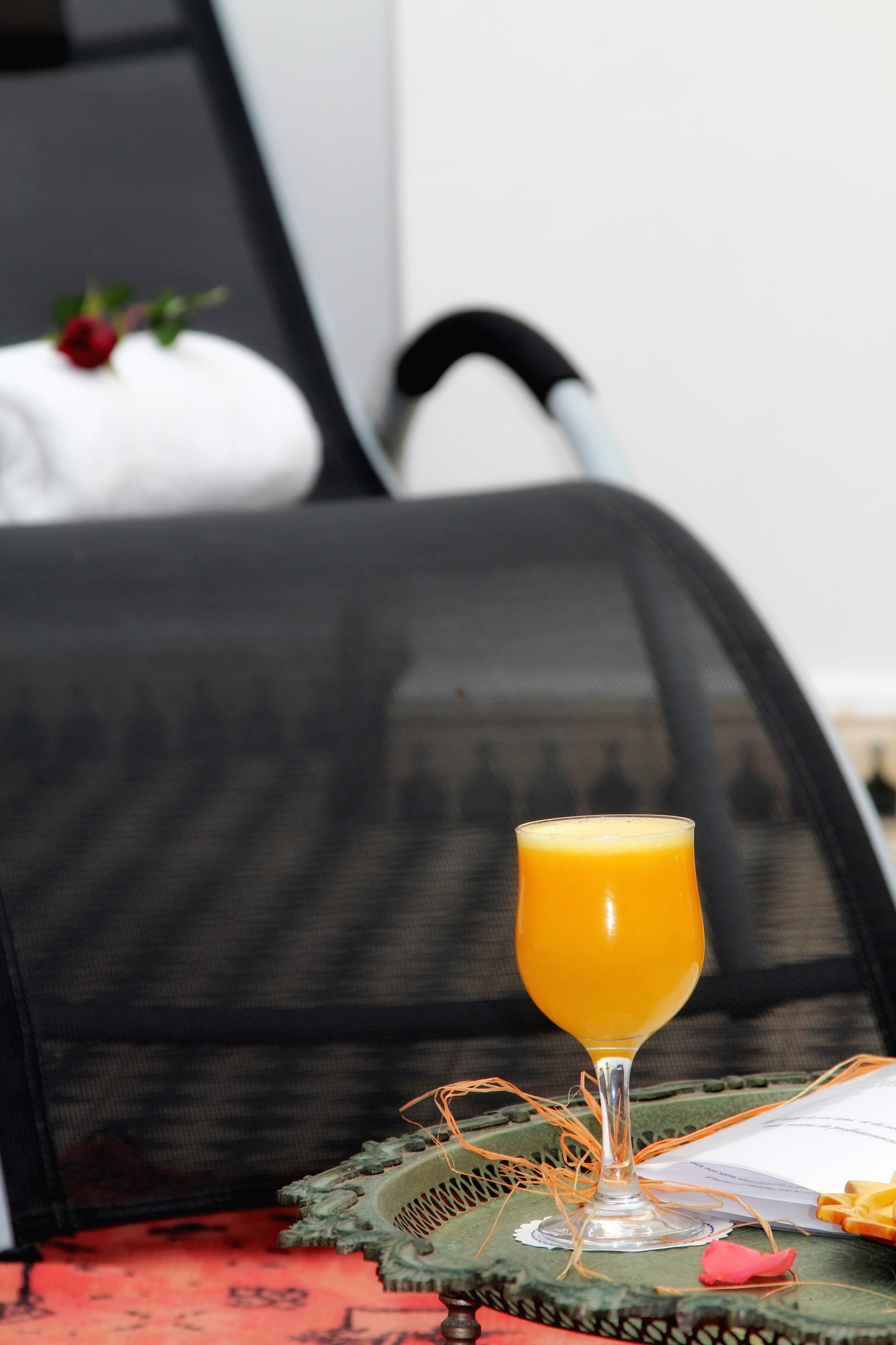 Un vaso de jugo de naranja sobre una bandeja con un plato decorativo, una libreta y un bolígrafo.