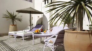 A sunlit patio with a checkered floor, lounge chairs, a table with fruit and drinks, and potted plants. - Casa Lila & Spa (Essaouira)