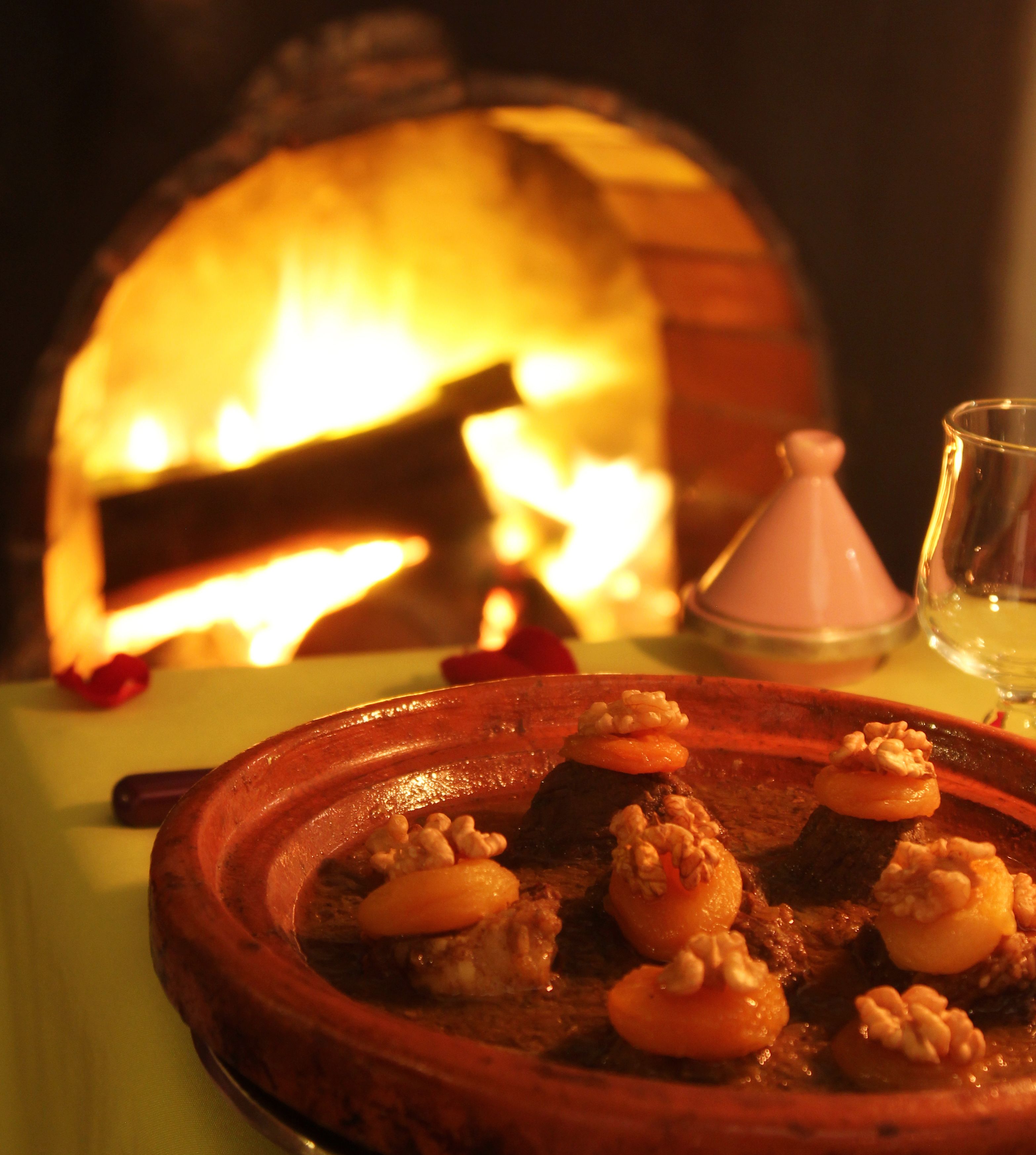 A dining table with a clay pot containing a stew, a glass of water, and a candle.