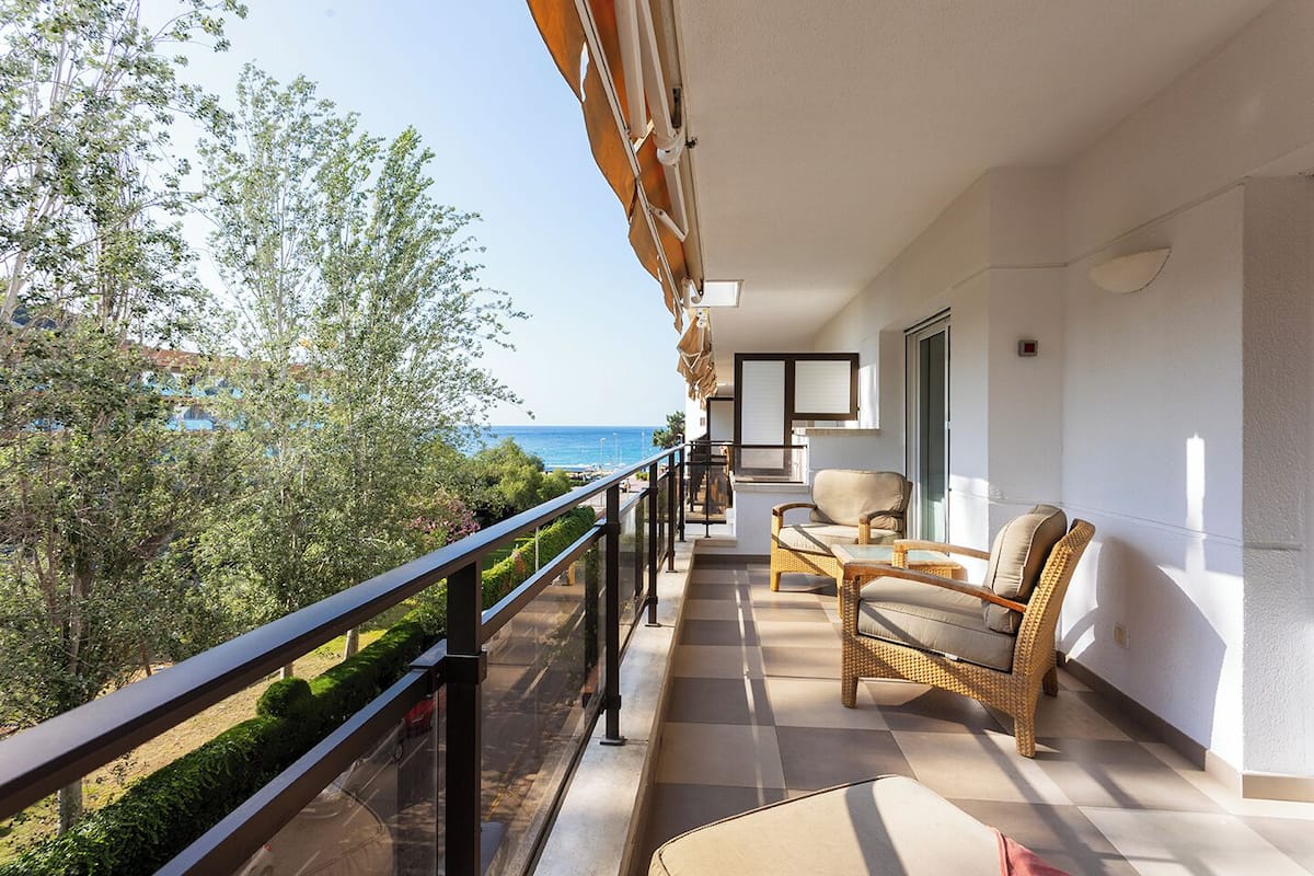 A balcony with wicker furniture, a view of the sea, and a clear sky.