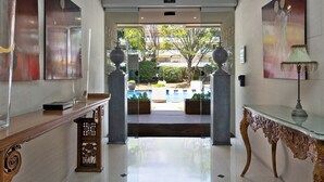 A hotel lobby with a polished floor, a reception desk, a decorative lamp, and a view of a pool area. - Suites del Mar Fenals (Lloret de Mar)