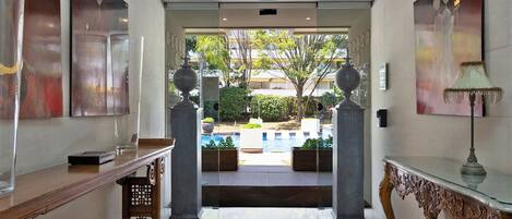 A hotel lobby with a polished floor, a reception desk, a decorative lamp, and a view of a pool area.