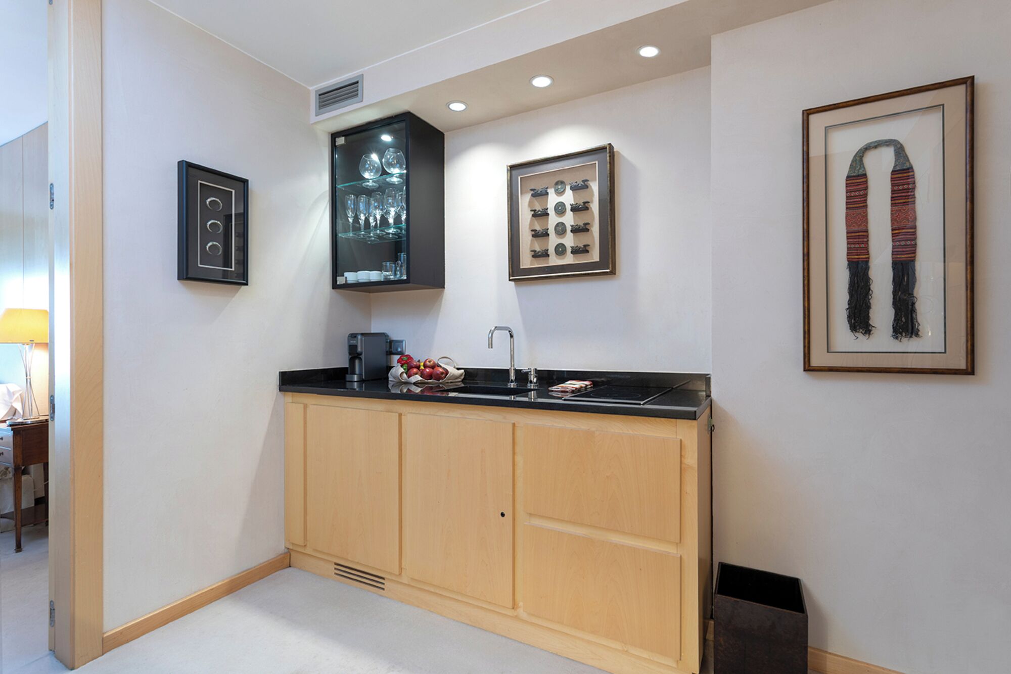 A modern kitchen with wooden cabinets, a black countertop, and a sink. There are framed pictures on the wall, including a pair of shoes and a decorative plate.
