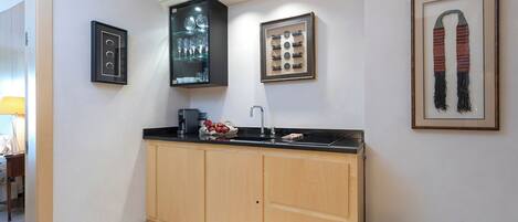 A modern kitchen with wooden cabinets, a black countertop, and a sink. There are framed pictures on the wall, including a pair of shoes and a decorative plate.