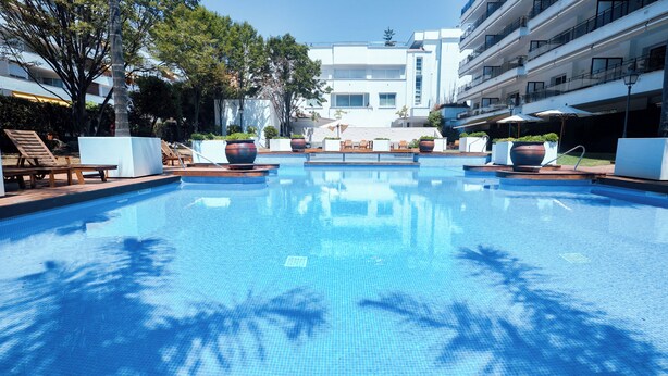 A swimming pool with lounge chairs and potted plants, surrounded by modern buildings. - Suites del Mar Fenals (Lloret de Mar)