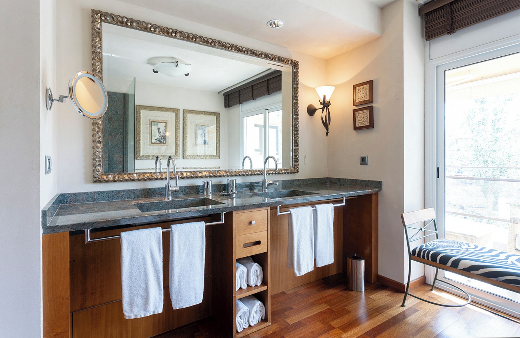 Un baño con un espejo grande, dos lavamanos, armarios de madera y una ventana con vistas.