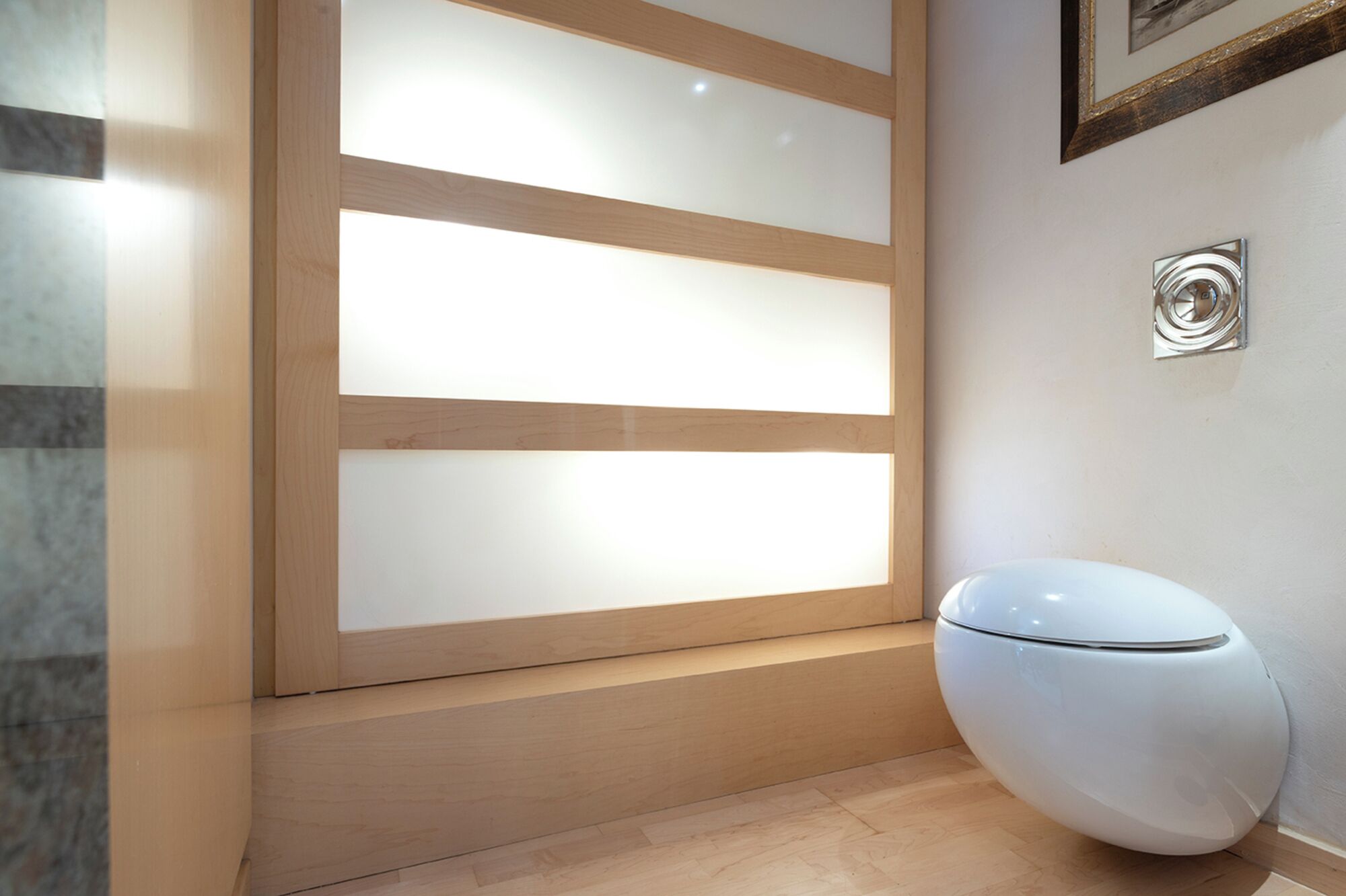 Un baño moderno con inodoro blanco, paneles de madera y un cuadro en la pared.