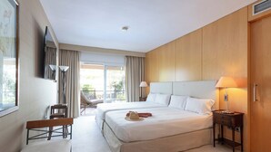 A hotel room with two beds, a bench, a chair, a TV, and a bedside table with a lamp. - Suites del Mar Fenals (Lloret de Mar)