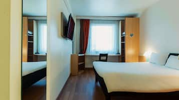 Una habitación de hotel con una cama grande, un escritorio, una silla, un televisor y un armario.