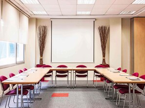 Un salón de conferencias con una pantalla grande, sillas rojas y una mesa larga.
