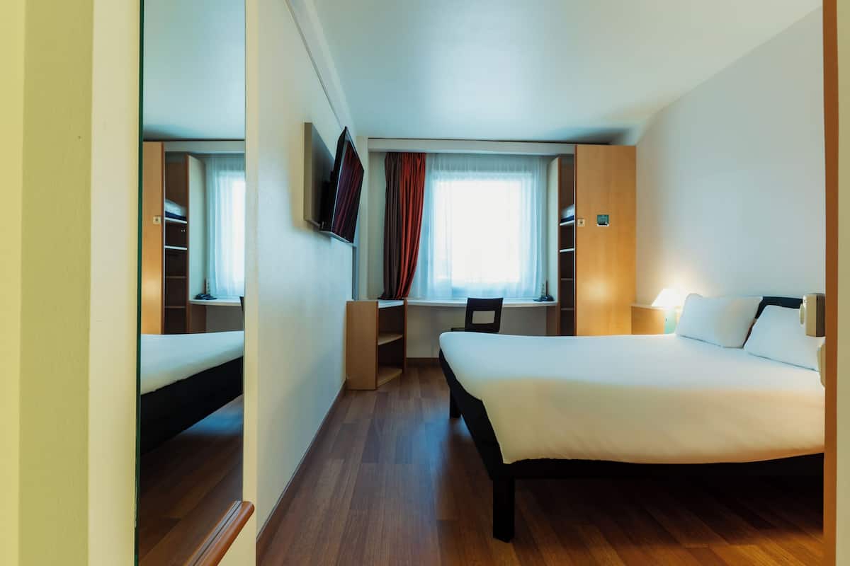 Une chambre d’hôtel équipée d’un lit, d’un bureau, d’une chaise et d’un téléviseur fixé au mur.