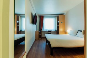 Une chambre d’hôtel équipée d’un lit, d’un bureau, d’une chaise et d’un téléviseur fixé au mur.