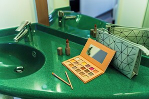 Un lavabo de salle de bain avec un plan de toilette vert, une palette de maquillage, deux pinceaux à maquillage et une trousse de toilette.