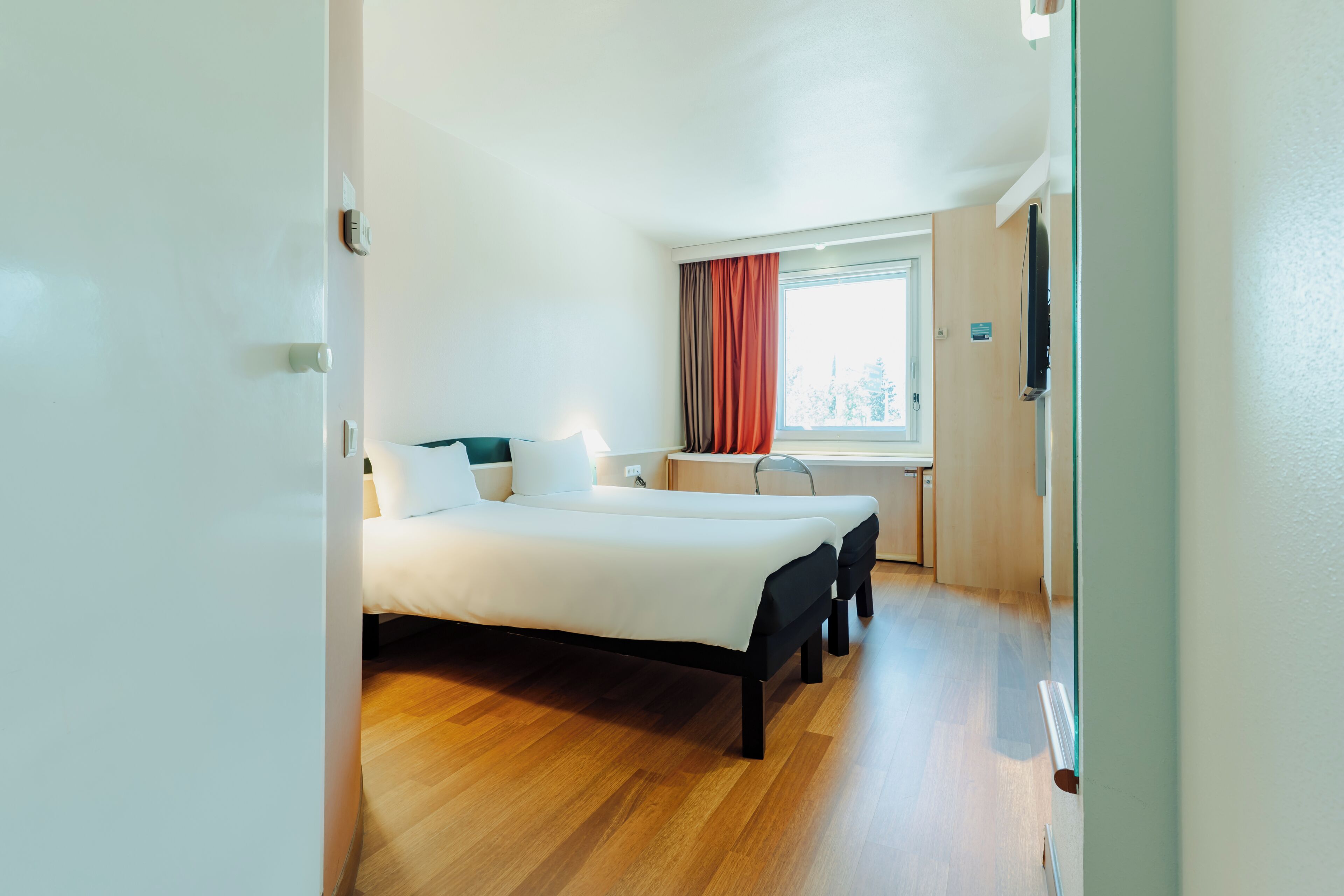 Een slaapkamer met een bed, nachtkastjes, een raam met gordijnen en een televisie.
