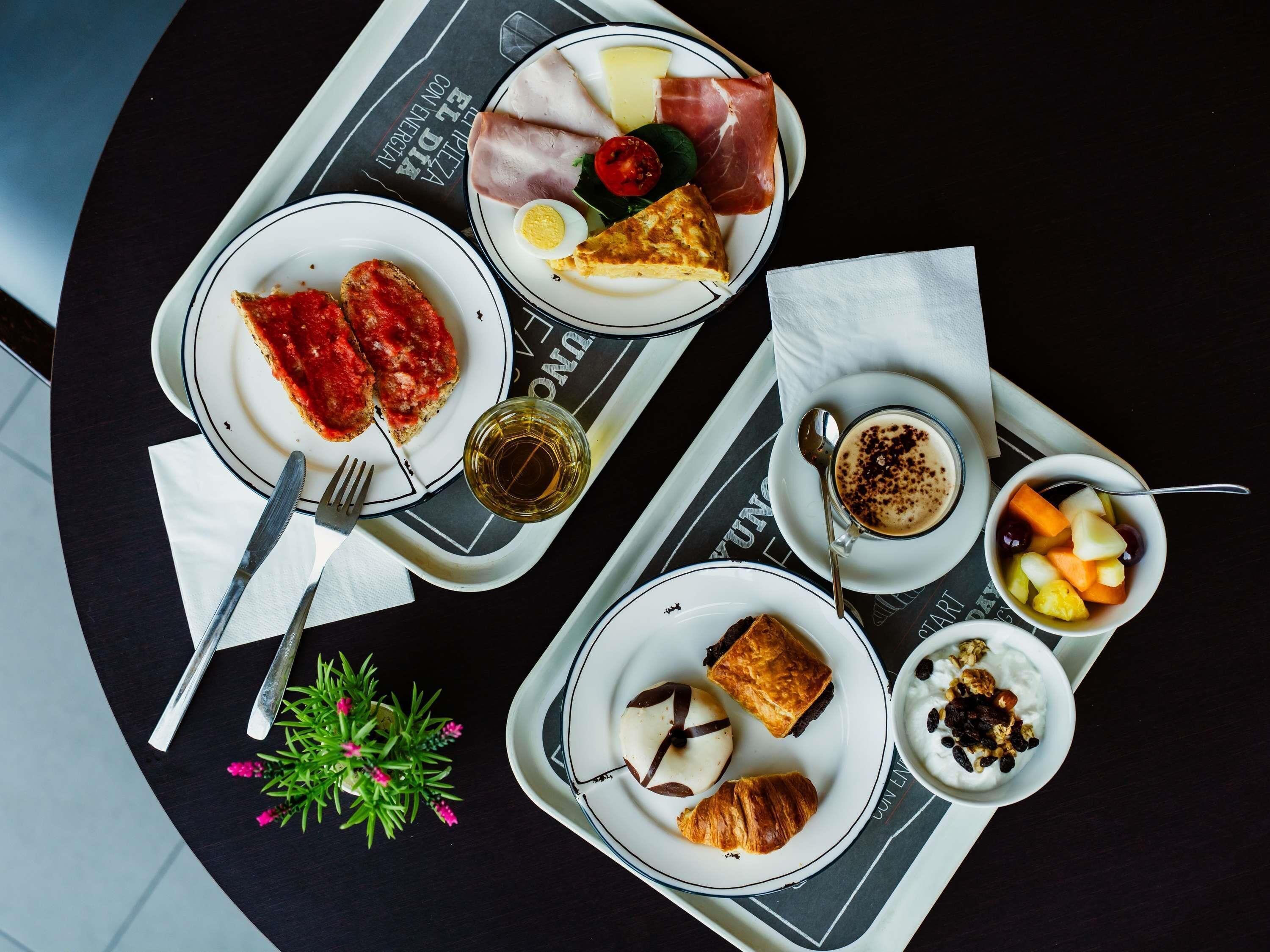 Une table à manger avec des assiettes remplies de nourriture, un verre de vin et une petite plante.