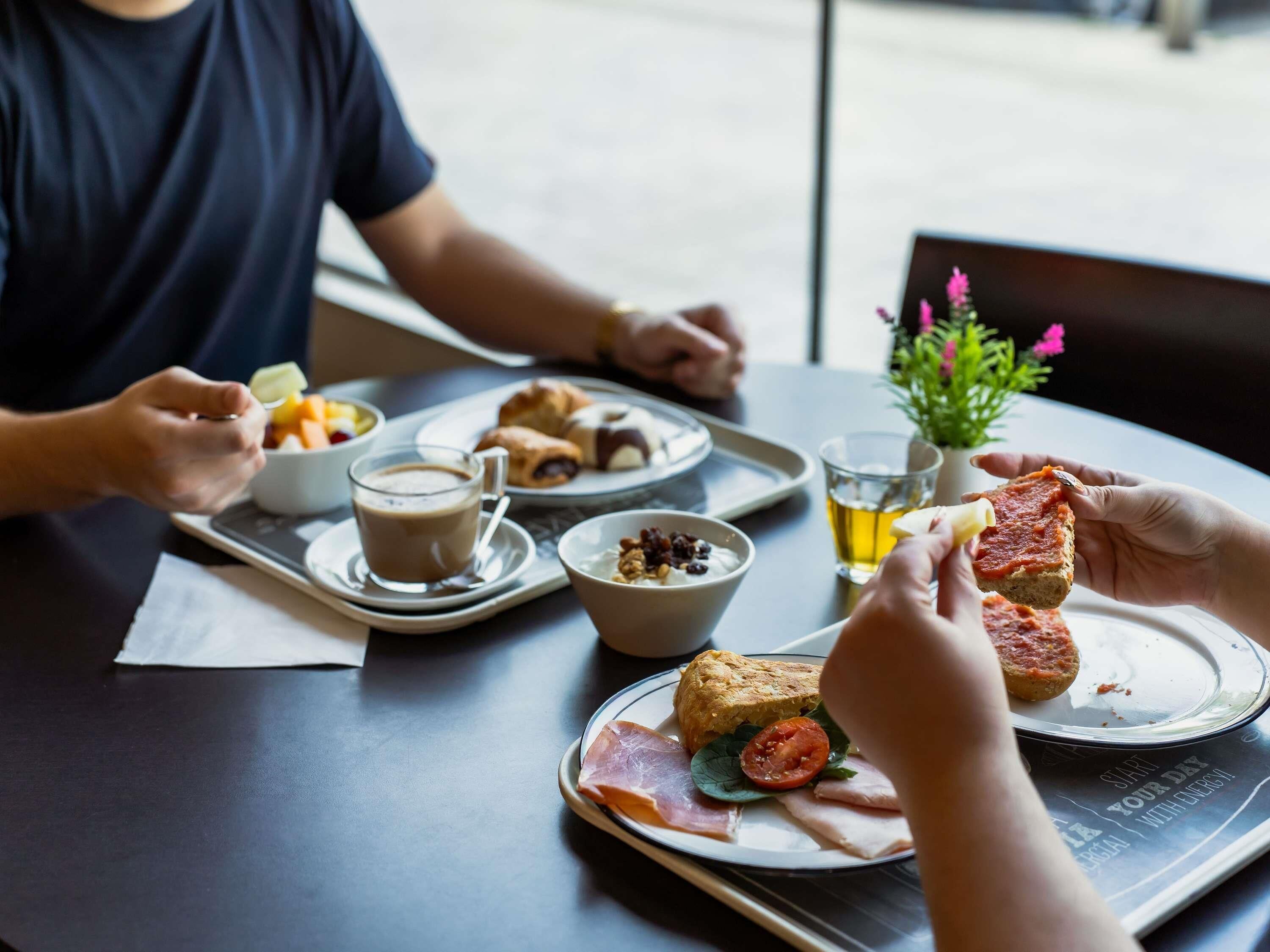A meal with bread, ham, tomato, and cheese on a plate, a cup of coffee, and a glass of beer on a tray.