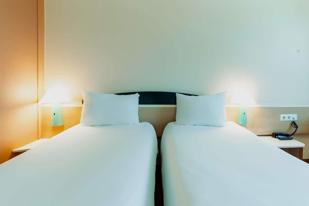 Une chambre d’hôtel avec deux lits, des lampes de chevet, une table de chevet avec un téléphone et une prise électrique au mur.