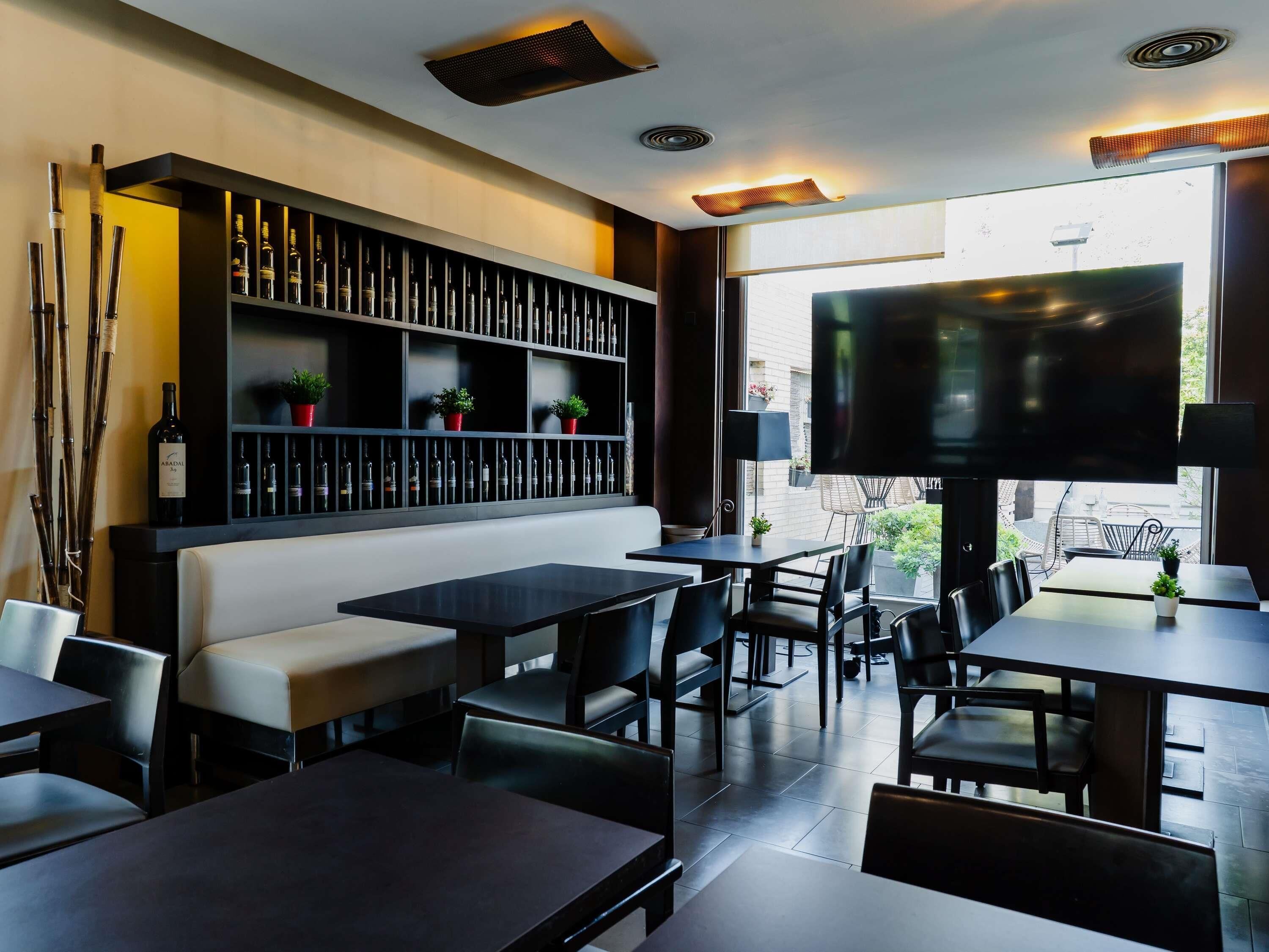 Un interior de restaurante con mesas, sillas, un sofá, un televisor y una estantería para vinos.