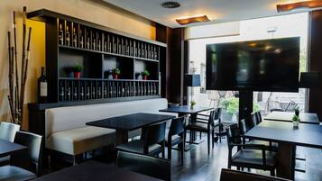 Un interior de restaurante con mesas, sillas, un sofá, un televisor y una estantería para vinos.