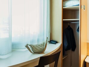 Una habitación con ventana, escritorio, silla, perchero y armario.