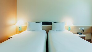 Habitación de hotel con dos camas, lámparas de noche, una mesita de noche y un enchufe en la pared.