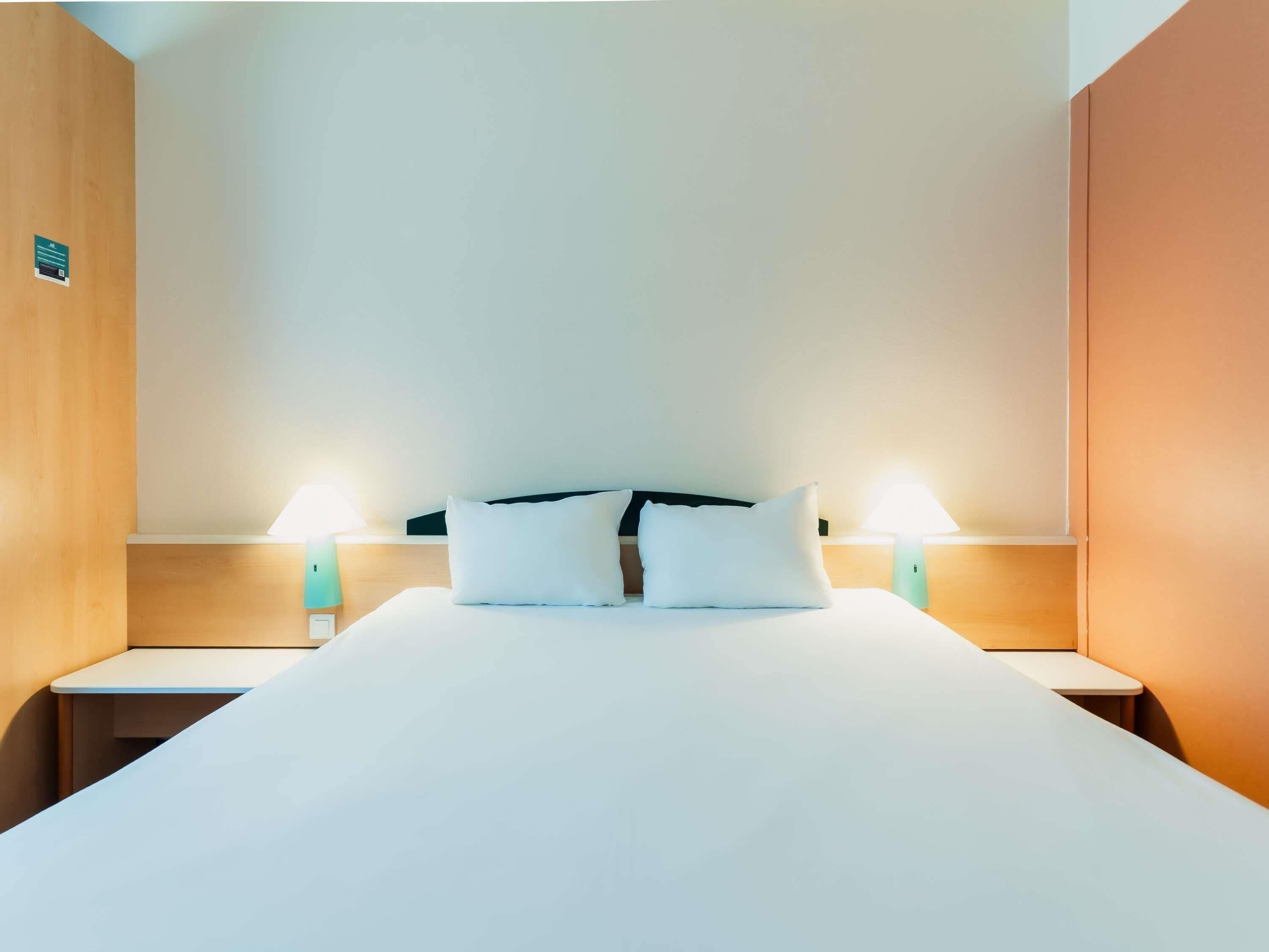 Una habitación de hotel con una cama grande, dos mesitas de noche y dos lámparas de pared.