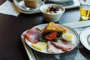 Un plato con diversos alimentos, incluyendo jamón, queso, un huevo duro y una rebanada de pan.