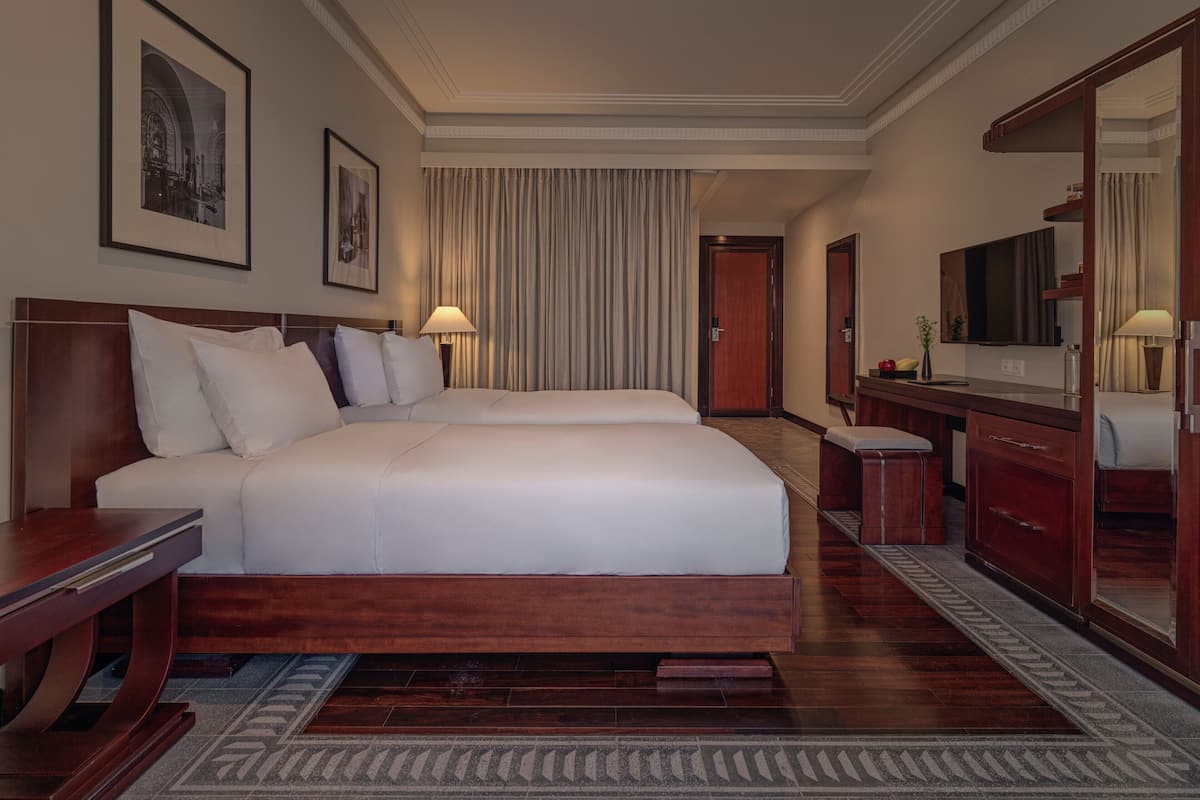 A hotel room with two beds, a large mirror, a desk, and a television.