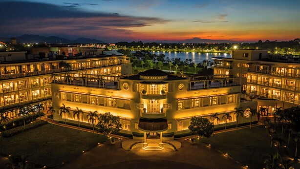 A multi-story hotel with a central courtyard, surrounded by a lake and mountains in the background. - Azerai La Residence Hue (Hue)