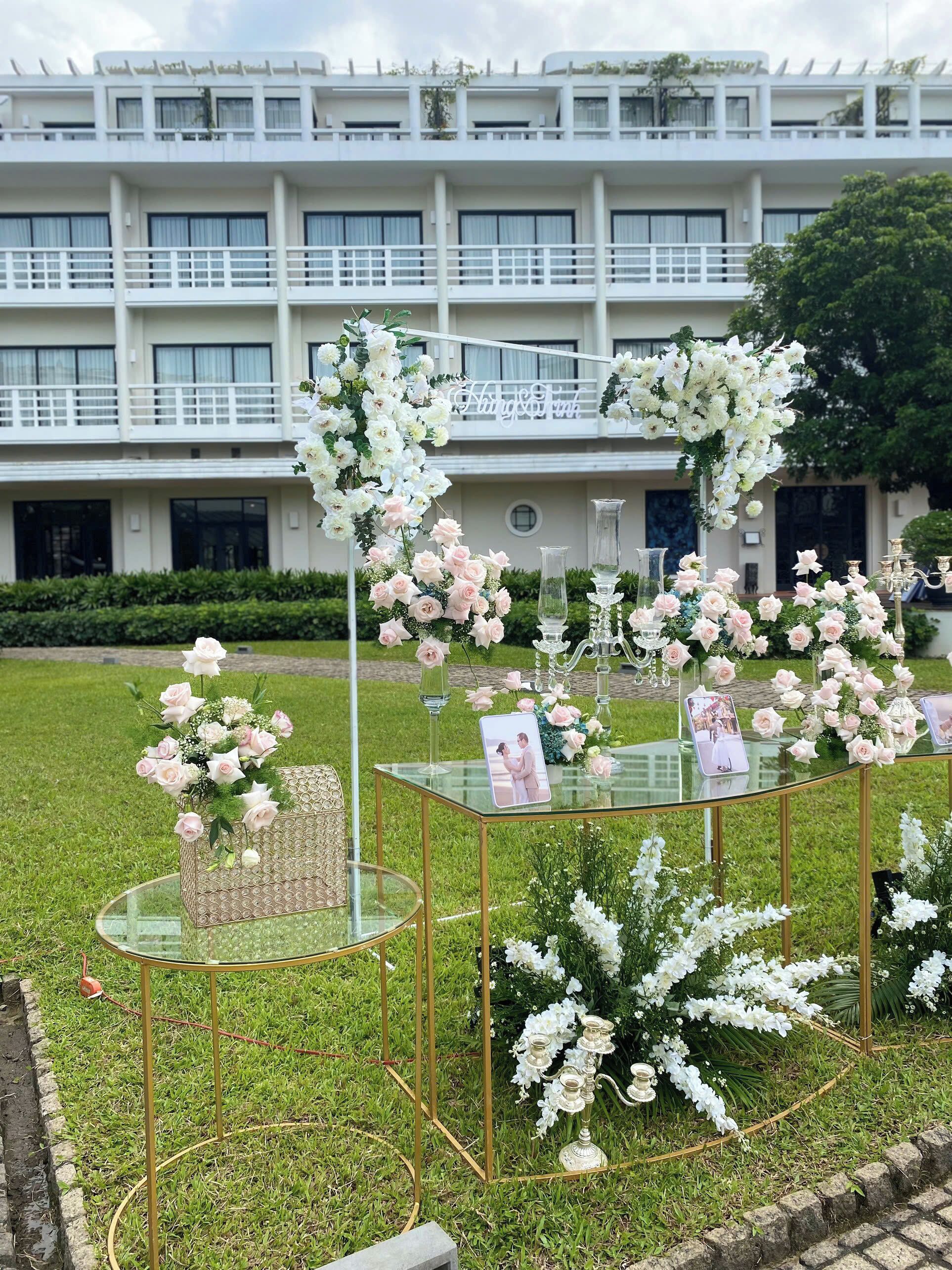 A wedding setup with floral arrangements and a glass table in front of a building.
