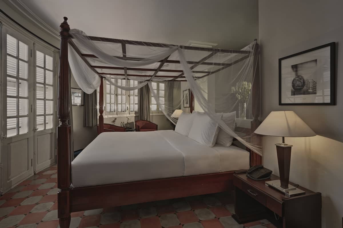 A four-poster bed with a canopy, a bedside table with a lamp, and a chair.
