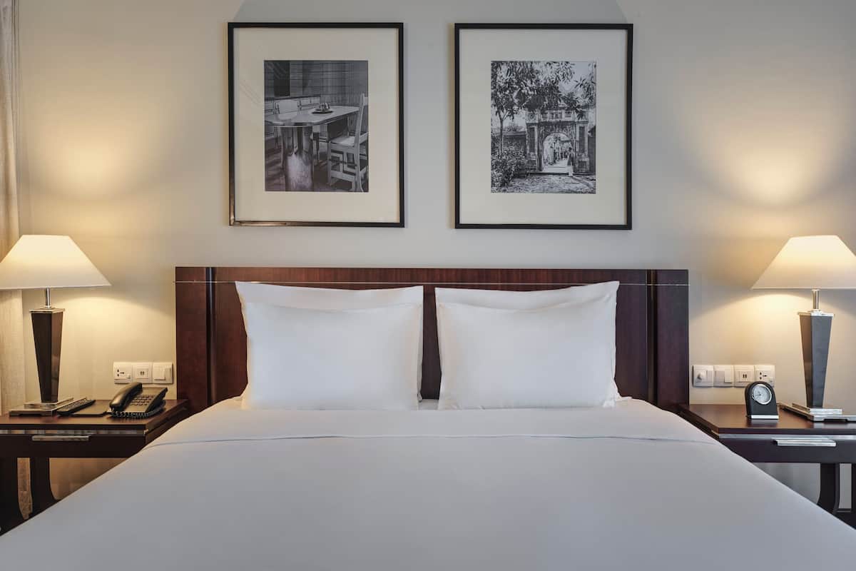 A hotel room with a large bed, two bedside tables, a nightstand, a lamp, a telephone, and two framed pictures on the wall.