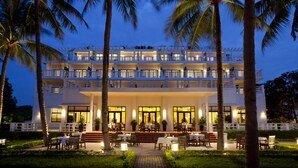 A multi-story hotel with outdoor seating and palm trees. - Azerai La Residence Hue (Hue)