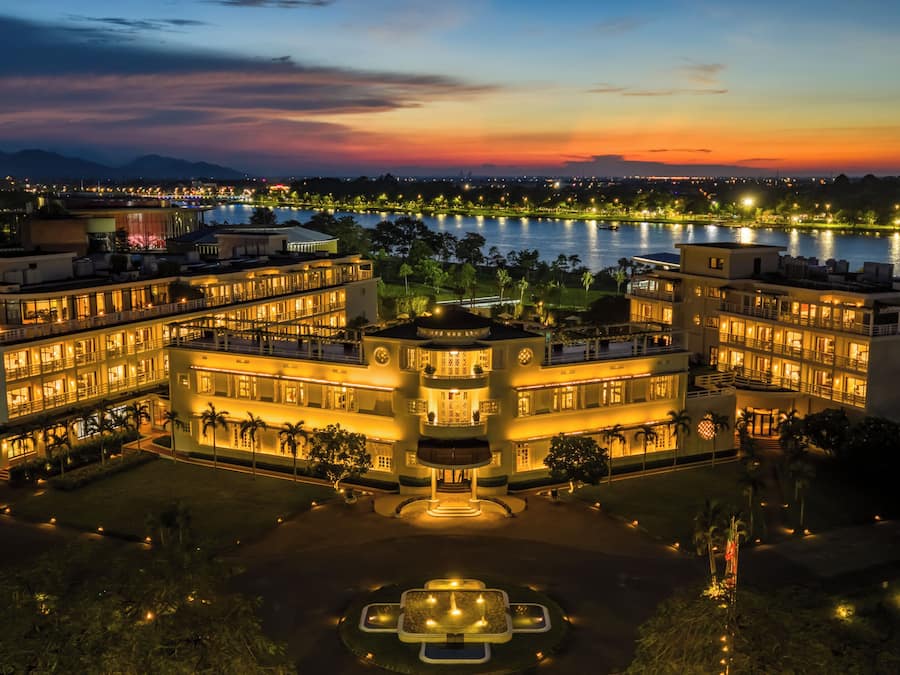 A multi-story hotel with a central courtyard, surrounded by water and mountains.