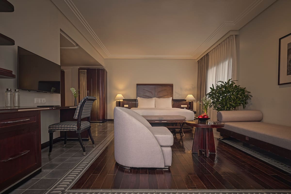 A hotel room with a bed, a sofa, a chair, a desk, and a large mirror.