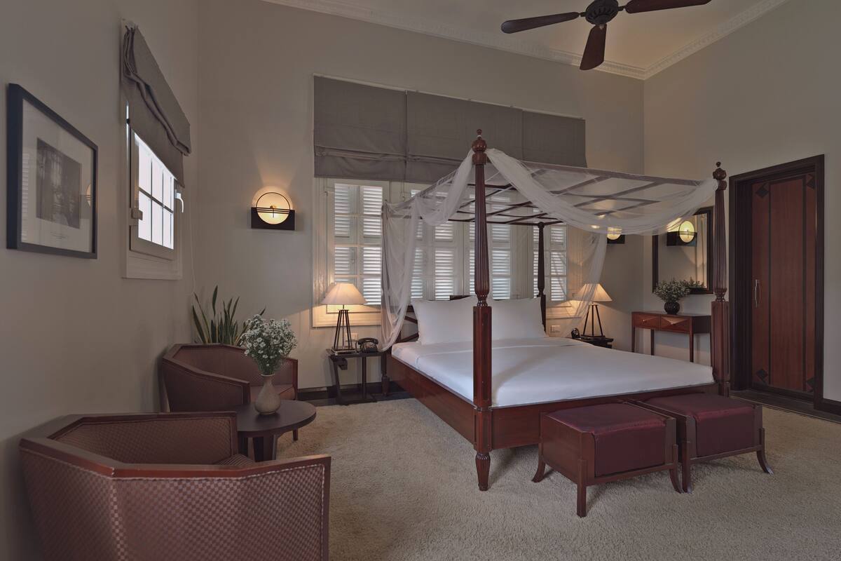 A four-poster bed with a canopy, a ceiling fan, and a large window with shutters.