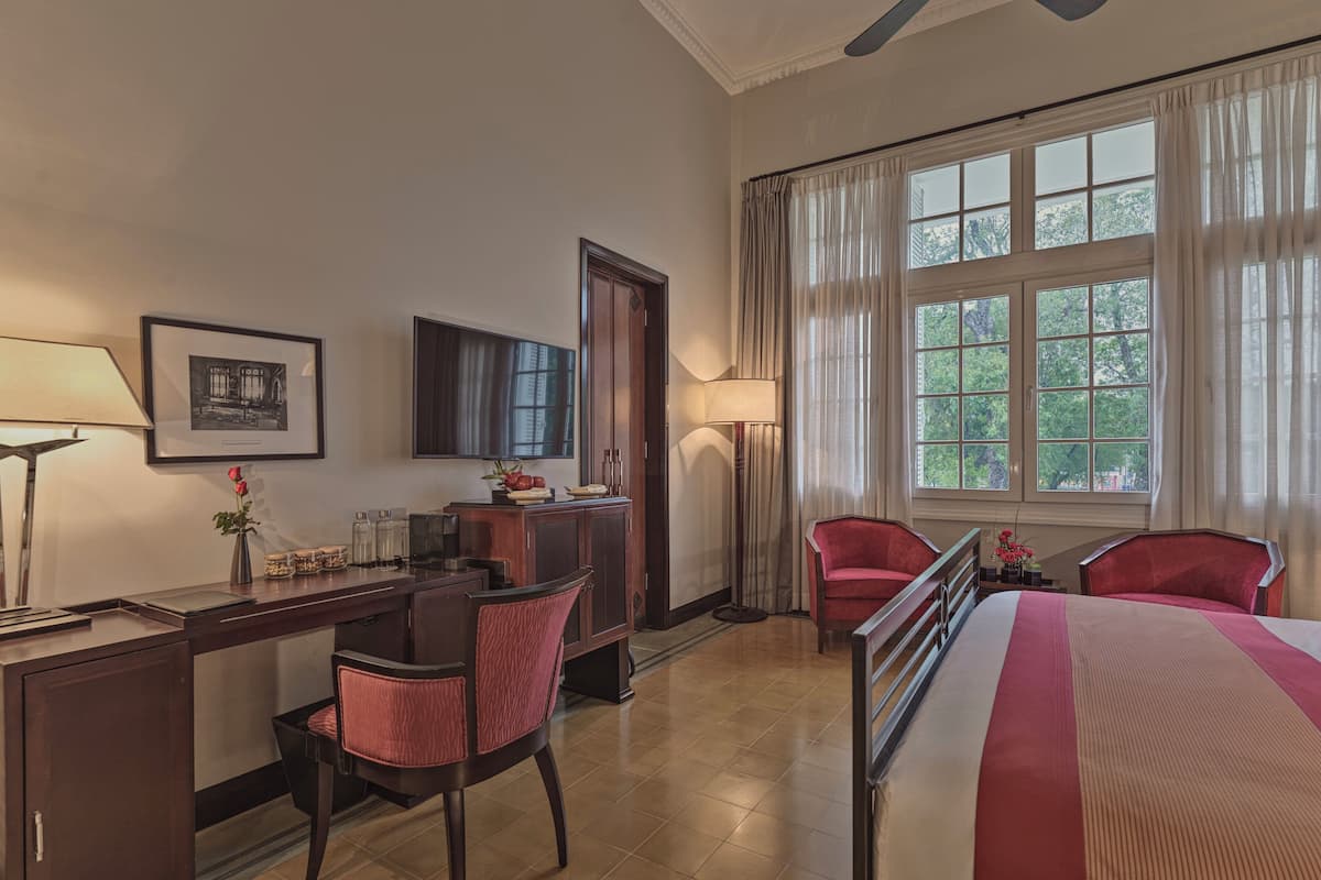 A hotel room with a desk, chairs, a bed, a TV, and a window with curtains.