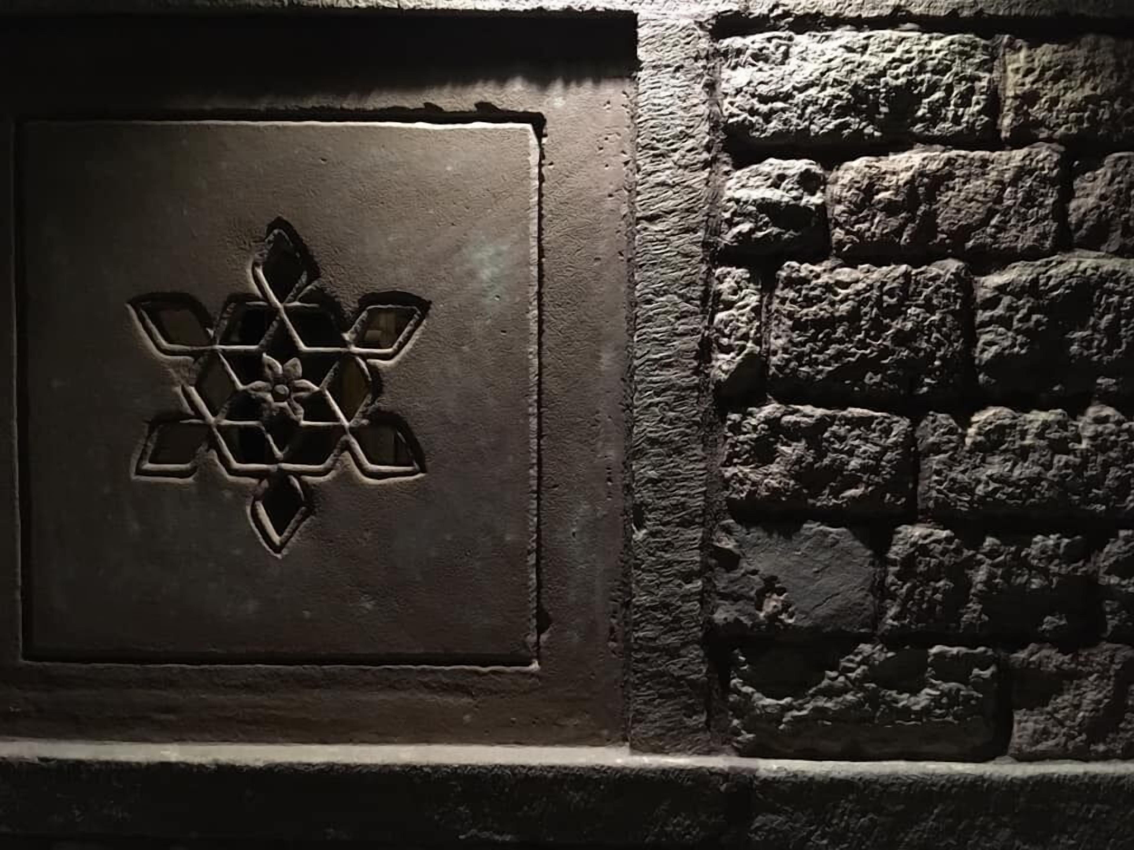 A stone wall with a metal panel featuring a geometric design.
